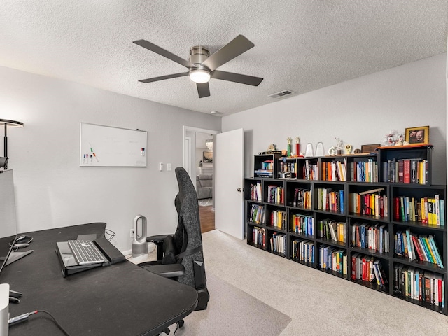 carpeted office space featuring ceiling fan and a textured ceiling