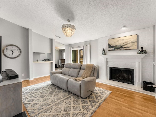 living room with a brick fireplace, an inviting chandelier, wood-type flooring, and lofted ceiling