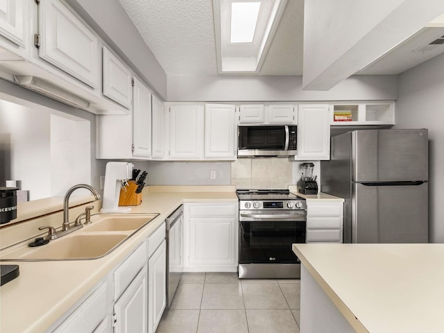 kitchen with tasteful backsplash, stainless steel appliances, white cabinets, light tile patterned floors, and sink