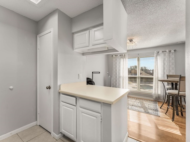 kitchen with white cabinets, light tile patterned floors, a textured ceiling, and kitchen peninsula