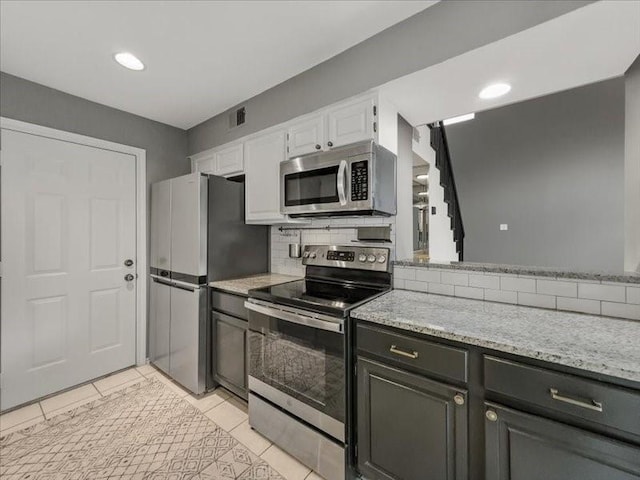 kitchen with white cabinetry, tasteful backsplash, light tile patterned floors, appliances with stainless steel finishes, and light stone countertops