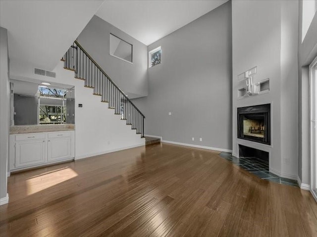 unfurnished living room with a high ceiling, plenty of natural light, and dark wood-type flooring