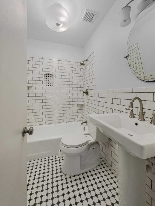 full bathroom featuring toilet, tiled shower / bath combo, sink, and tile walls