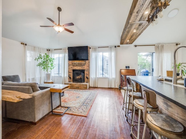 living room with ceiling fan, vaulted ceiling with beams, hardwood / wood-style floors, and a fireplace