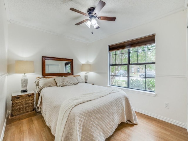 bedroom featuring ceiling fan, ornamental molding, a textured ceiling, and light wood-type flooring