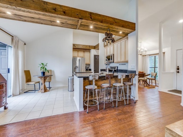 kitchen with lofted ceiling with beams, a breakfast bar area, a chandelier, stainless steel appliances, and light wood-type flooring