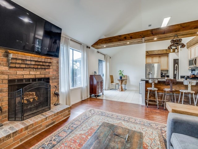 living room featuring light hardwood / wood-style floors, lofted ceiling with beams, and a brick fireplace