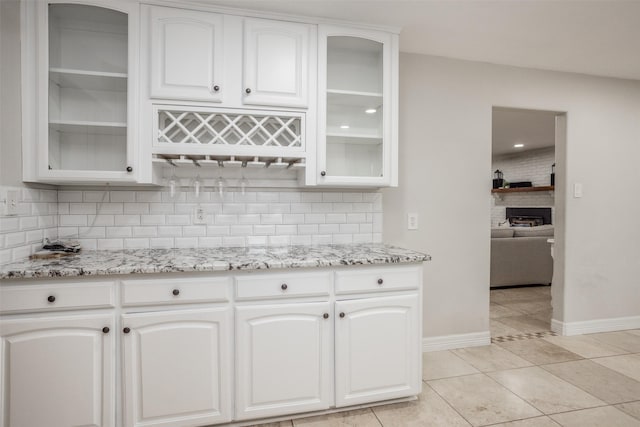 kitchen featuring white cabinetry, backsplash, a fireplace, and light stone countertops