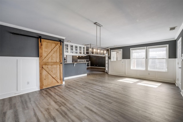 unfurnished living room featuring hardwood / wood-style floors, ornamental molding, and a barn door