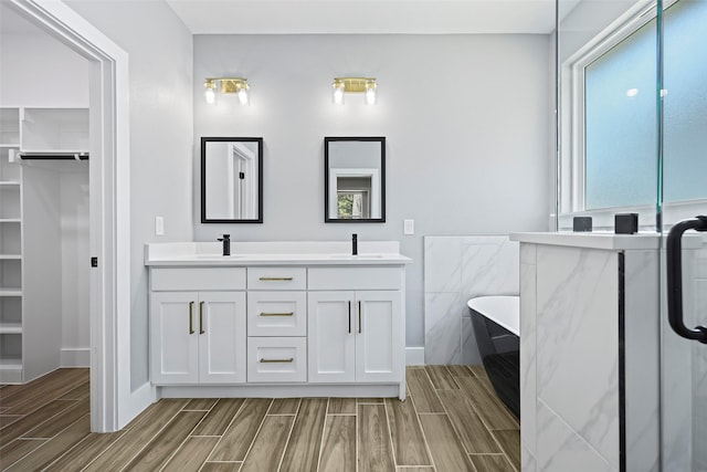 11298 Cedar Dr, Mabank, TX 75156 - bathroom featuring wood tiled floors, double vanity, a walk in closet, a soaking tub, and baseboards
