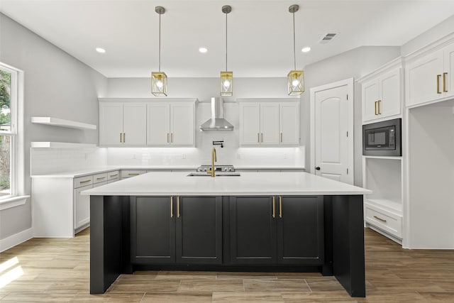 kitchen with a kitchen island with sink, white cabinets, built in microwave, and wall chimney exhaust hood