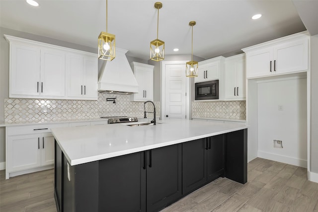 kitchen featuring sink, a center island with sink, black microwave, pendant lighting, and white cabinets