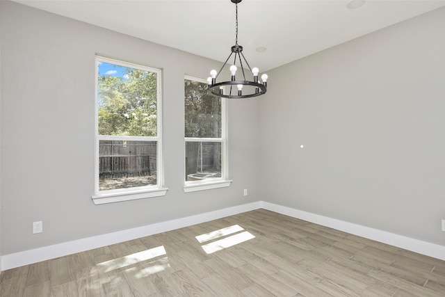 unfurnished room featuring a notable chandelier and light wood-type flooring