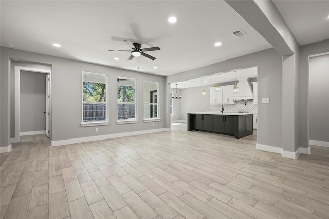 unfurnished living room with sink, ceiling fan with notable chandelier, and light wood-type flooring