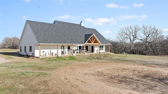 rear view of house featuring a shingled roof, a chimney, a porch, and a yard