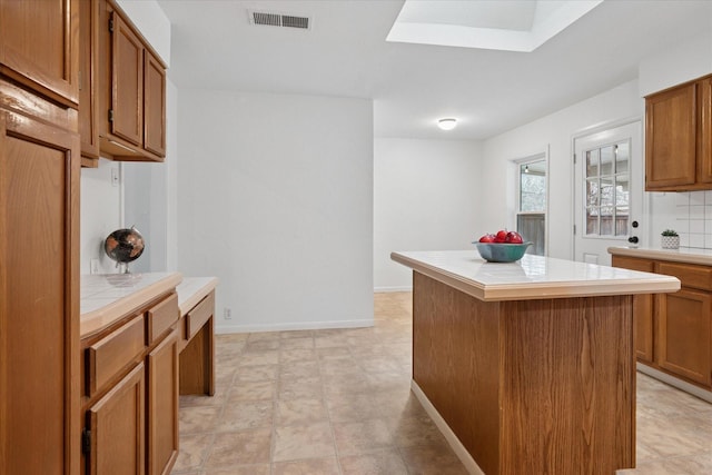 kitchen featuring a skylight, tile countertops, visible vents, brown cabinetry, and a kitchen island