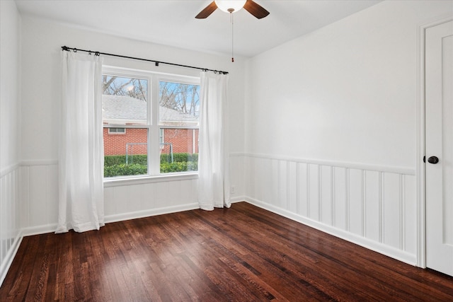 unfurnished room featuring a wainscoted wall, ceiling fan, and dark wood-style flooring