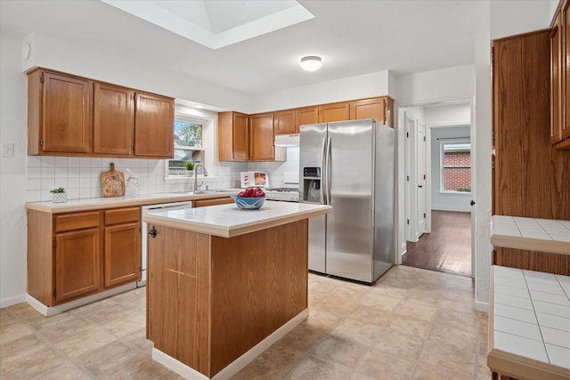 kitchen featuring brown cabinets, backsplash, a kitchen island, and stainless steel fridge with ice dispenser