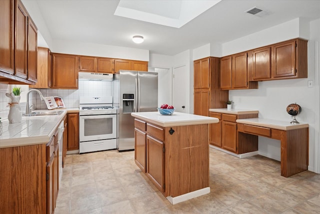 kitchen featuring white gas stove, light countertops, a sink, under cabinet range hood, and stainless steel fridge with ice dispenser