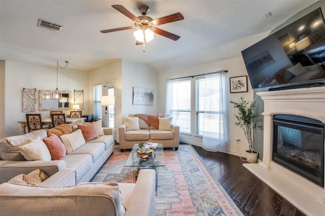 living area with visible vents, a ceiling fan, a glass covered fireplace, wood finished floors, and baseboards