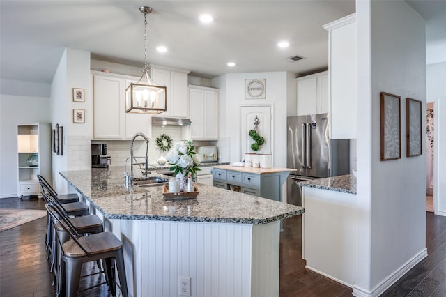 kitchen with a peninsula, a sink, white cabinets, hanging light fixtures, and dark stone countertops