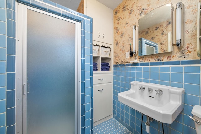 bathroom with toilet, a wainscoted wall, a sink, tile walls, and wallpapered walls