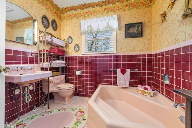 bathroom with a wainscoted wall, a garden tub, toilet, and wallpapered walls