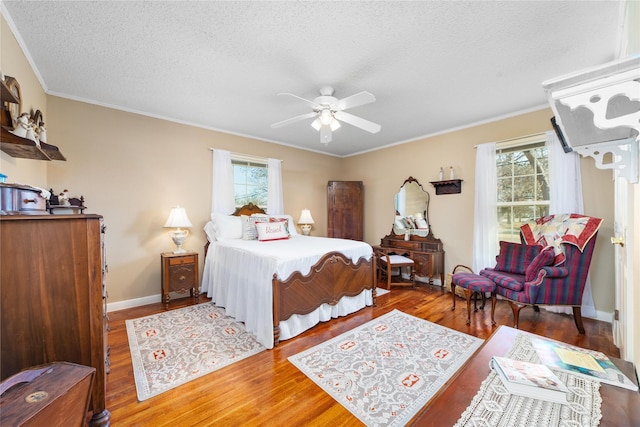 bedroom with a textured ceiling, multiple windows, wood finished floors, and baseboards