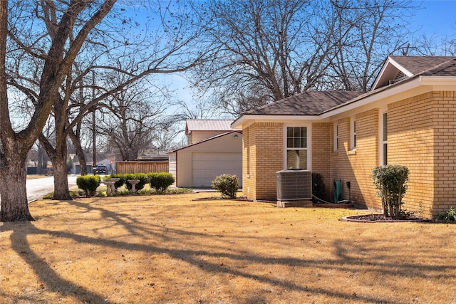 view of side of home with a garage, brick siding, a yard, and central AC