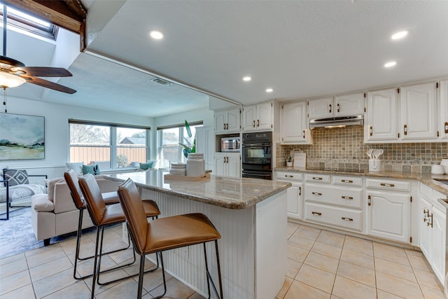 kitchen with a breakfast bar area, light stone counters, black appliances, white cabinets, and decorative backsplash