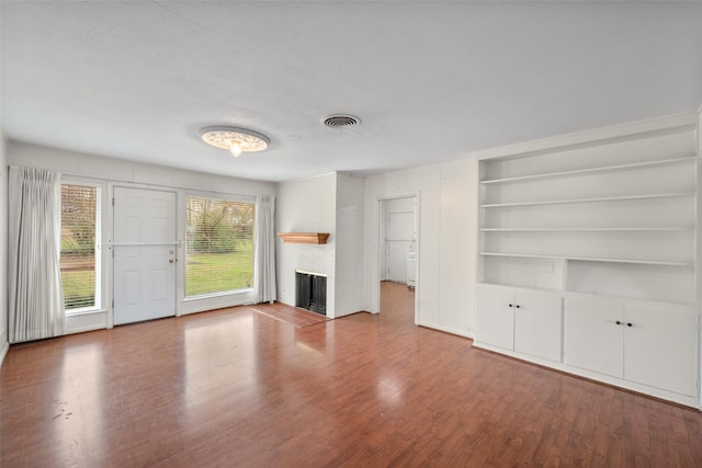 unfurnished living room featuring hardwood / wood-style floors, built in shelves, and a fireplace