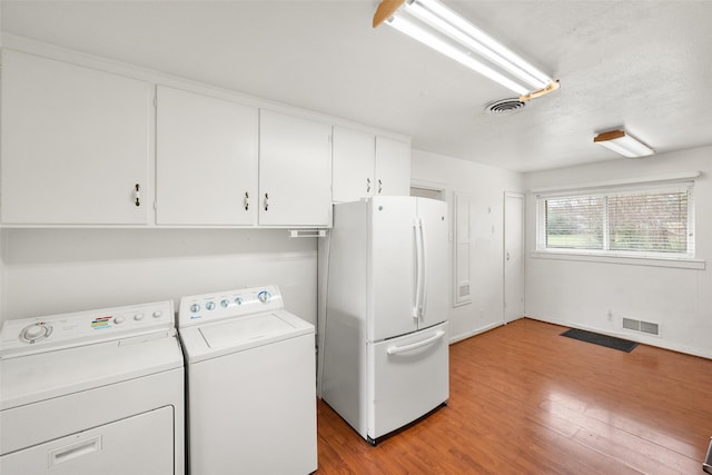 laundry area with washing machine and dryer, cabinets, and light wood-type flooring