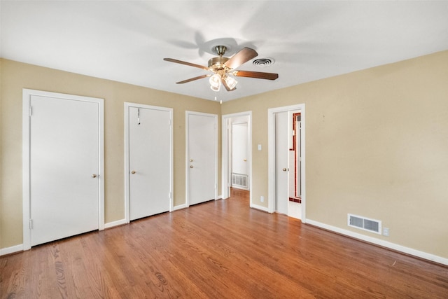 unfurnished bedroom with ceiling fan, two closets, and light wood-type flooring