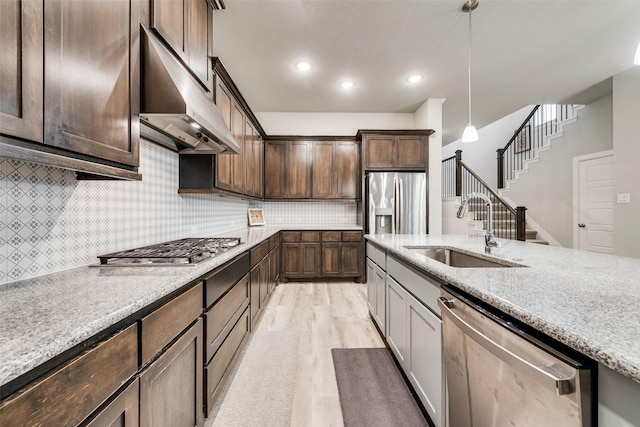 kitchen with dark brown cabinetry, stainless steel appliances, light stone countertops, and sink