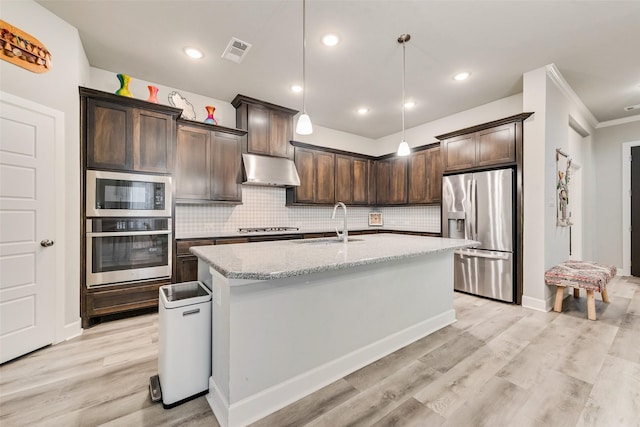 kitchen with a center island with sink, hanging light fixtures, stainless steel appliances, light stone counters, and sink