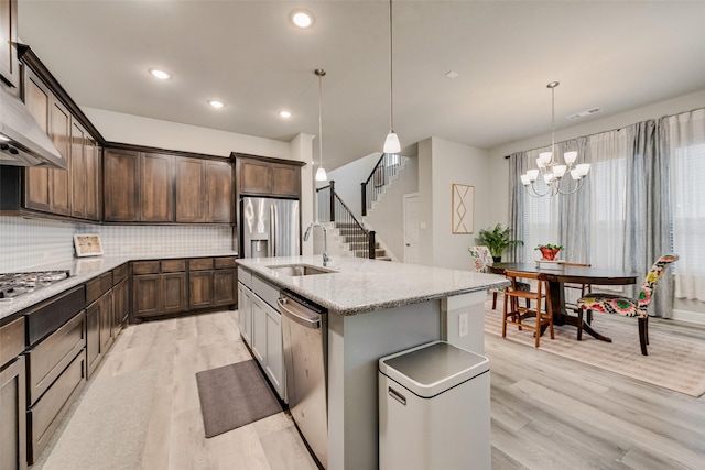 kitchen with an island with sink, hanging light fixtures, dark brown cabinetry, sink, and appliances with stainless steel finishes