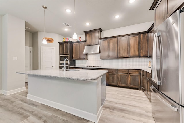 kitchen with a center island with sink, appliances with stainless steel finishes, sink, light stone counters, and pendant lighting