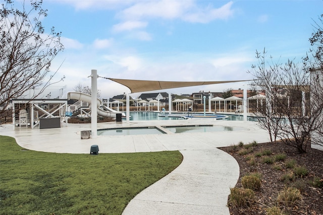 pool with a patio area, a water slide, a hot tub, and a lawn