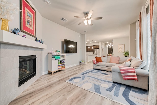 living room with light wood-type flooring, a fireplace, and ceiling fan with notable chandelier