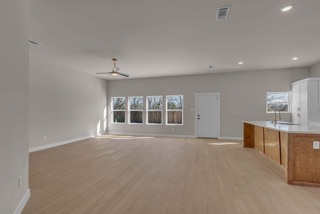 unfurnished living room featuring ceiling fan, plenty of natural light, sink, and light wood-type flooring