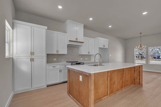 kitchen with sink, white cabinetry, stainless steel range, a center island with sink, and decorative light fixtures