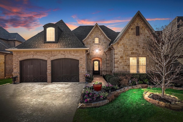 french country home featuring an attached garage, brick siding, concrete driveway, and roof with shingles