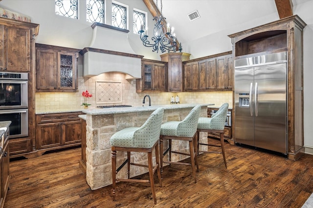 kitchen with dark brown cabinetry, visible vents, dark wood finished floors, light stone counters, and stainless steel appliances