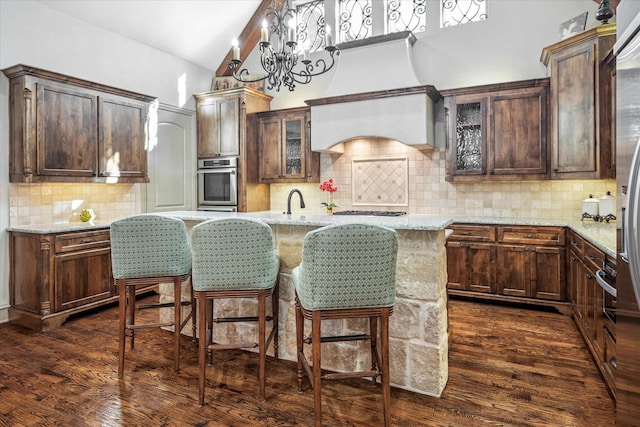 kitchen featuring a kitchen island with sink, light stone counters, dark wood-style flooring, and stainless steel oven