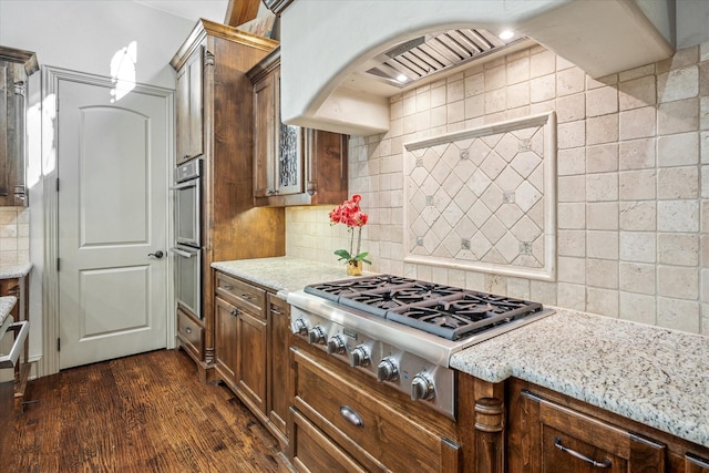 kitchen featuring stainless steel gas cooktop, custom range hood, decorative backsplash, dark wood-type flooring, and light stone countertops