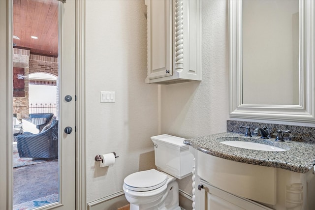 half bathroom featuring a textured wall, vanity, and toilet