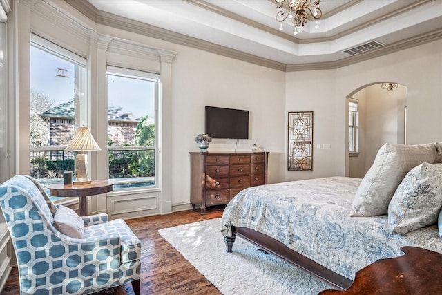 bedroom featuring arched walkways, wood finished floors, visible vents, ornamental molding, and a tray ceiling