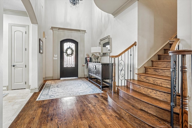 foyer featuring arched walkways, crown molding, a towering ceiling, wood finished floors, and stairs