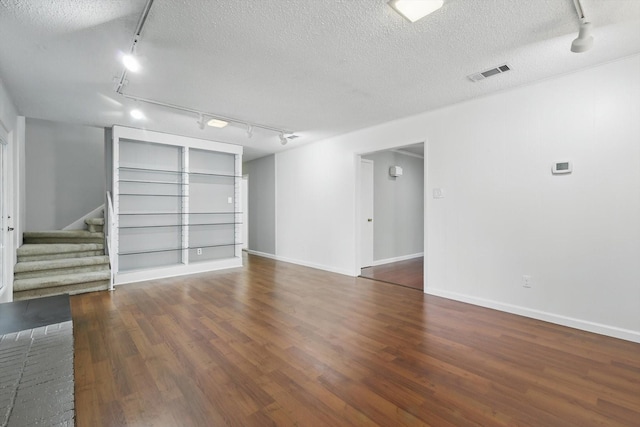 unfurnished room featuring stairs, a textured ceiling, visible vents, and wood finished floors