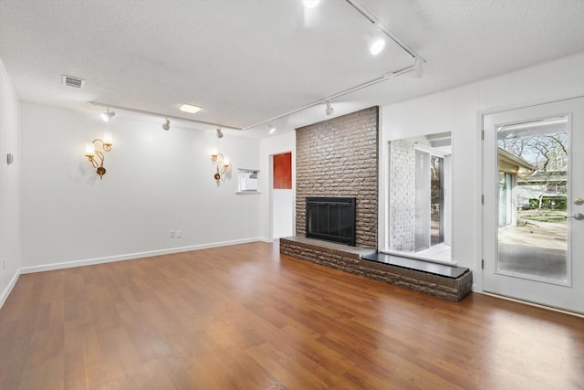 unfurnished living room with a textured ceiling, a brick fireplace, wood finished floors, and visible vents